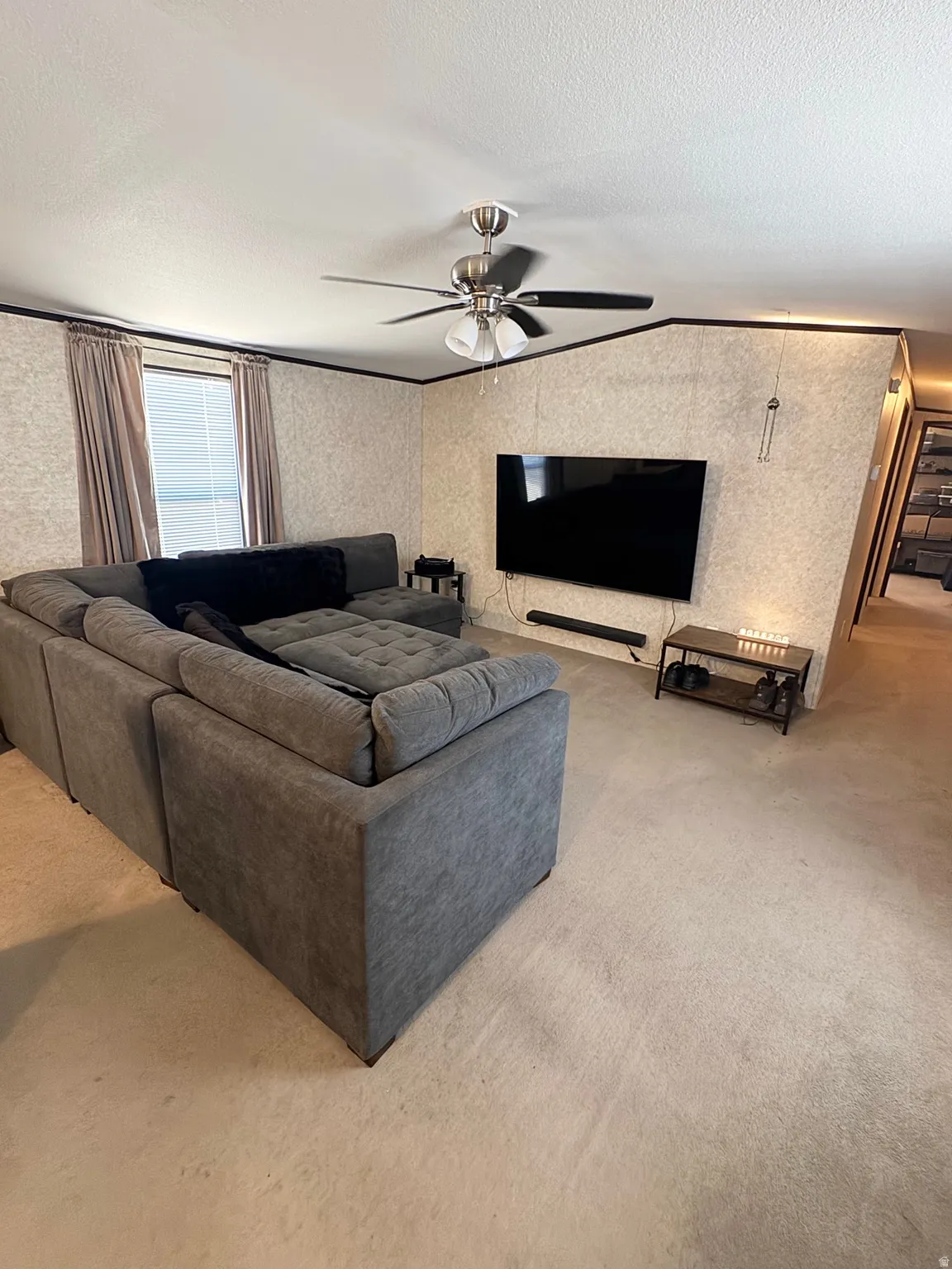 Living area featuring light-colored carpet, textured wall finishes, and a ceiling fan with integrated lighting