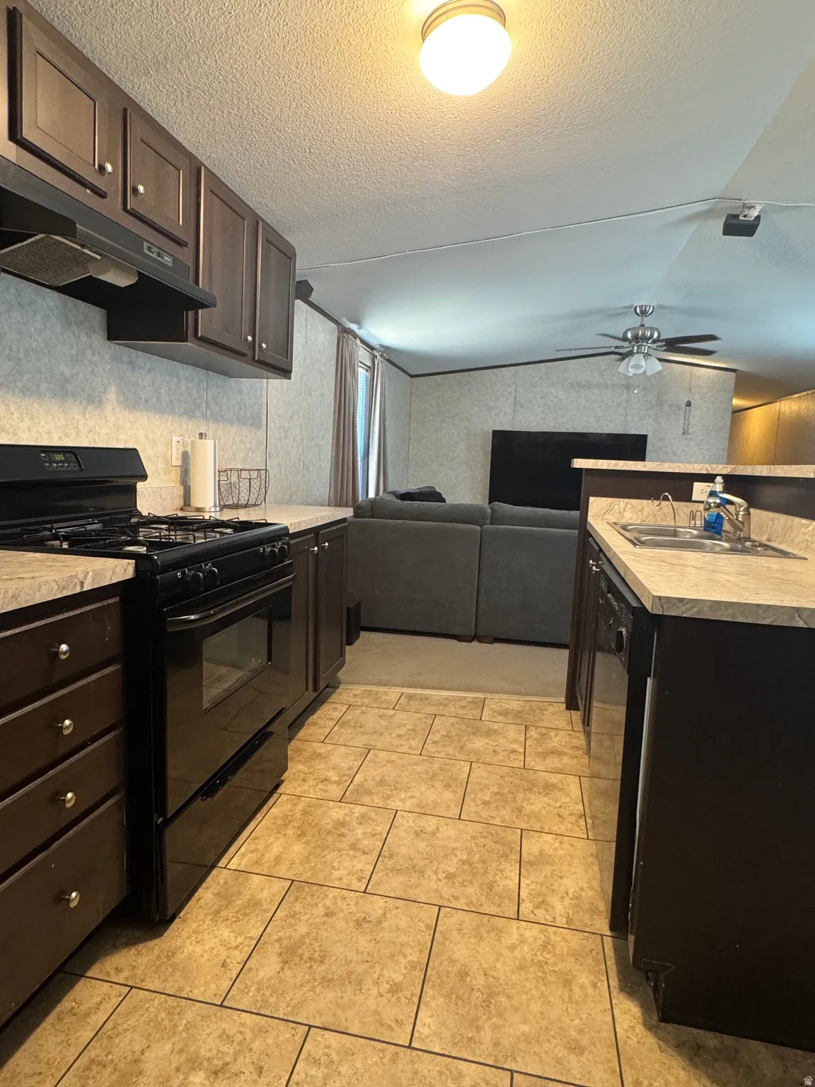 Kitchen featuring a black range and matching overhead microwave, dark wood-finish cabinetry, and light-toned countertops