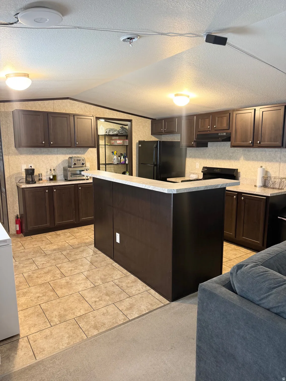 Spacious kitchen featuring dark wood-finish cabinetry, a central island with countertop, and tile flooring