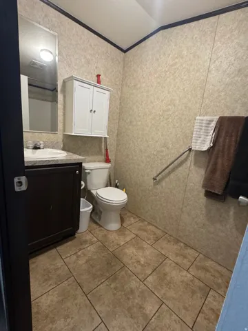 Bathroom featuring a dark wood-finish vanity with a white countertop and integrated sink, a wall-mounted mirror, a white two-door storage cabinet, and large-format tile flooring
