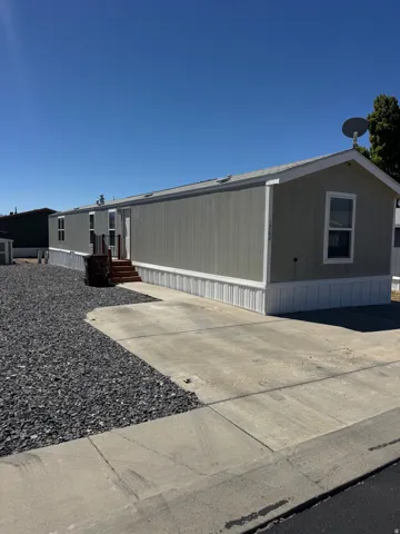 Single-story residence featuring light gray siding with white trim, a gabled roofline, and a concrete driveway