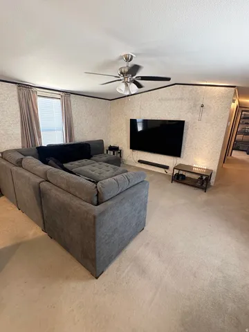 Living area featuring light-colored carpet, textured wall finishes, and a ceiling fan with integrated lighting