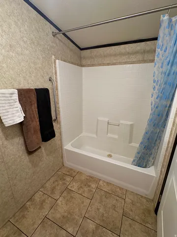 Bathroom featuring a white bathtub with integrated shower, white subway tile-style surround, and a grab bar