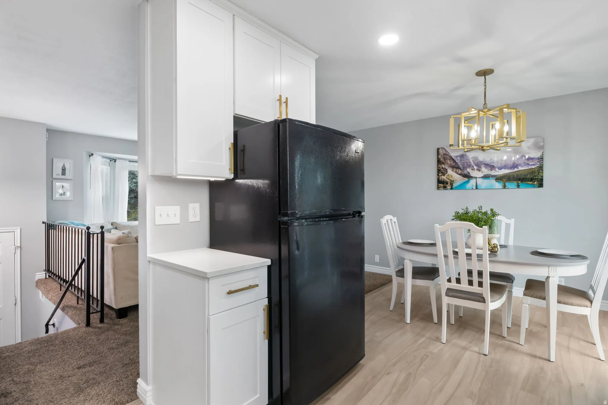 Dining area featuring wood-finish flooring, a contemporary chandelier, and a built-in cabinet with white shaker-style doors and gold-finish hardware