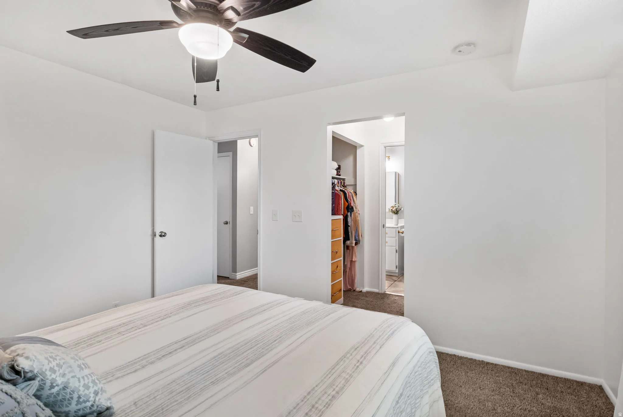 Bedroom featuring a ceiling fan with light fixture, neutral carpeting, white walls, and a doorway leading to a walk-in closet