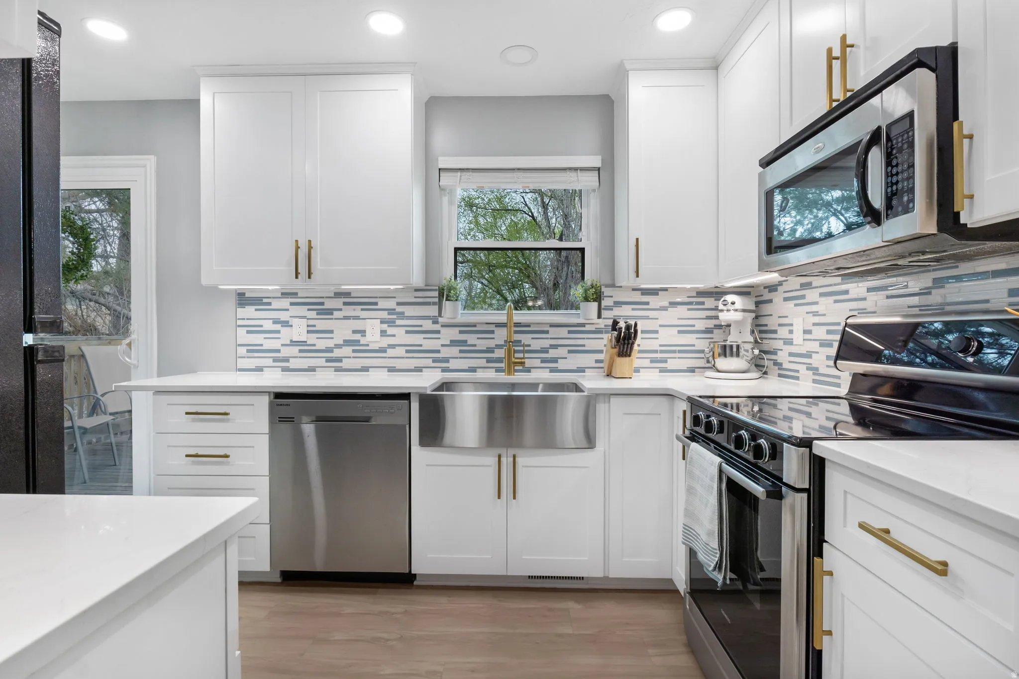 Bright kitchen featuring white cabinetry with gold-tone hardware, stainless steel appliances, and a unique horizontal tile backsplash