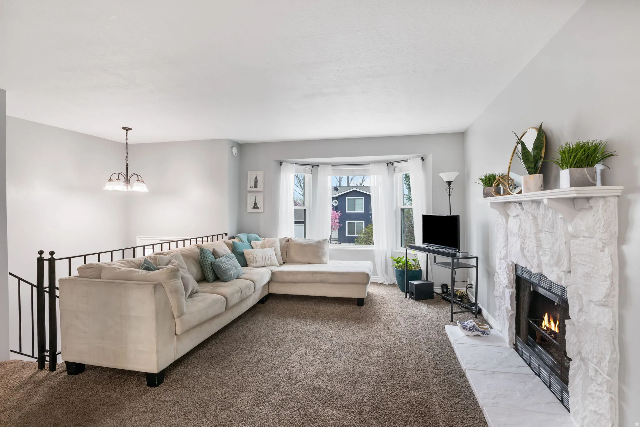 Living area featuring a stone-clad fireplace with a hearth, bay windows, and a carpeted floor
