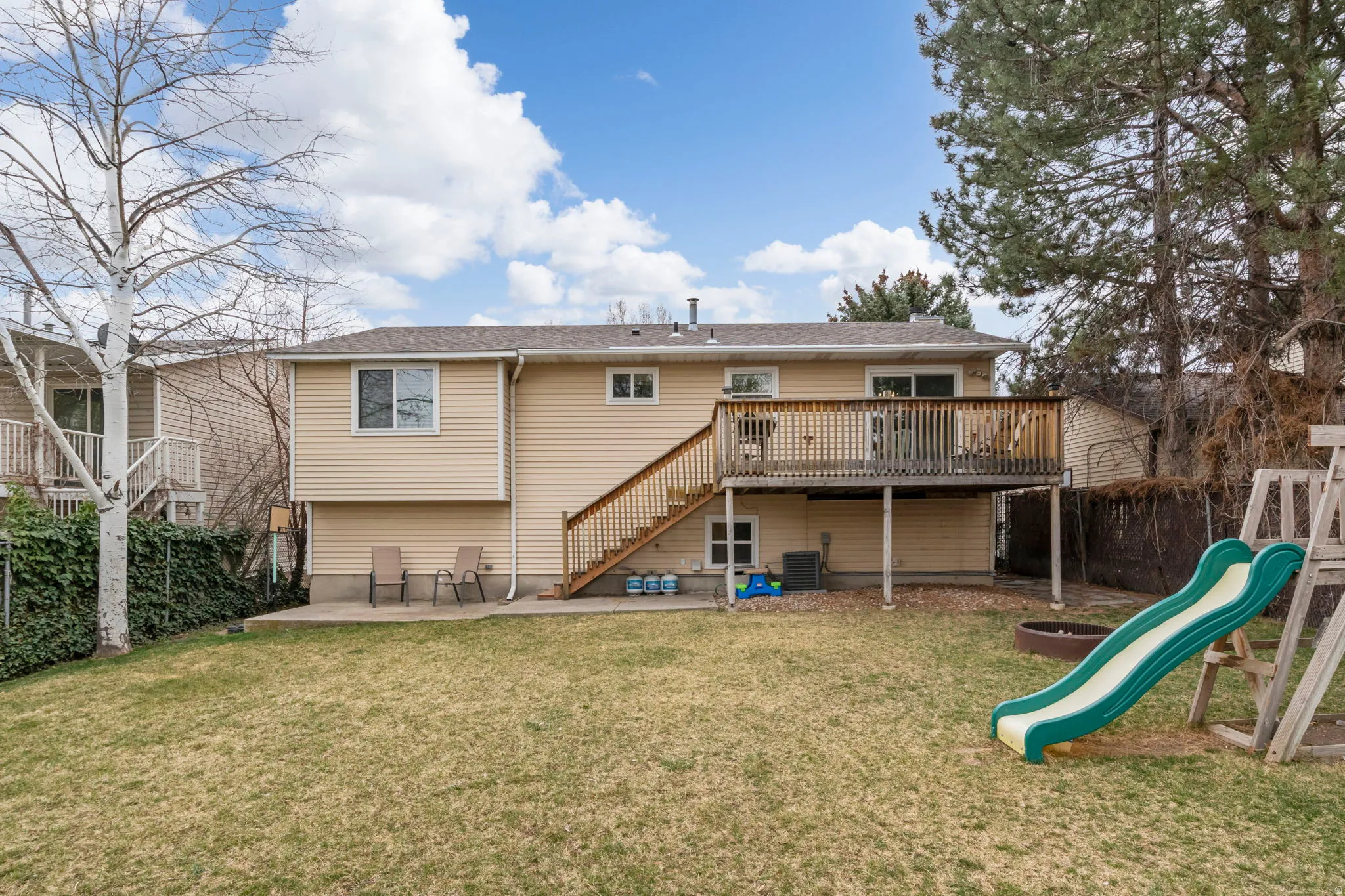 Backyard featuring a wooden deck with railing, stairs, and a ground-level concrete patio