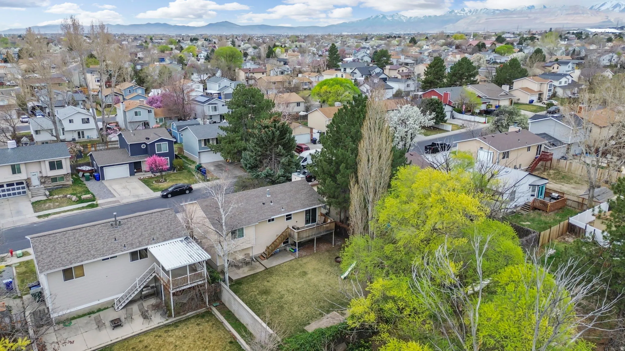 Aerial perspective of a neighborhood featuring a single-family residence with a neutral-toned exterior, a sloped shingle roof, and a backyard with a deck