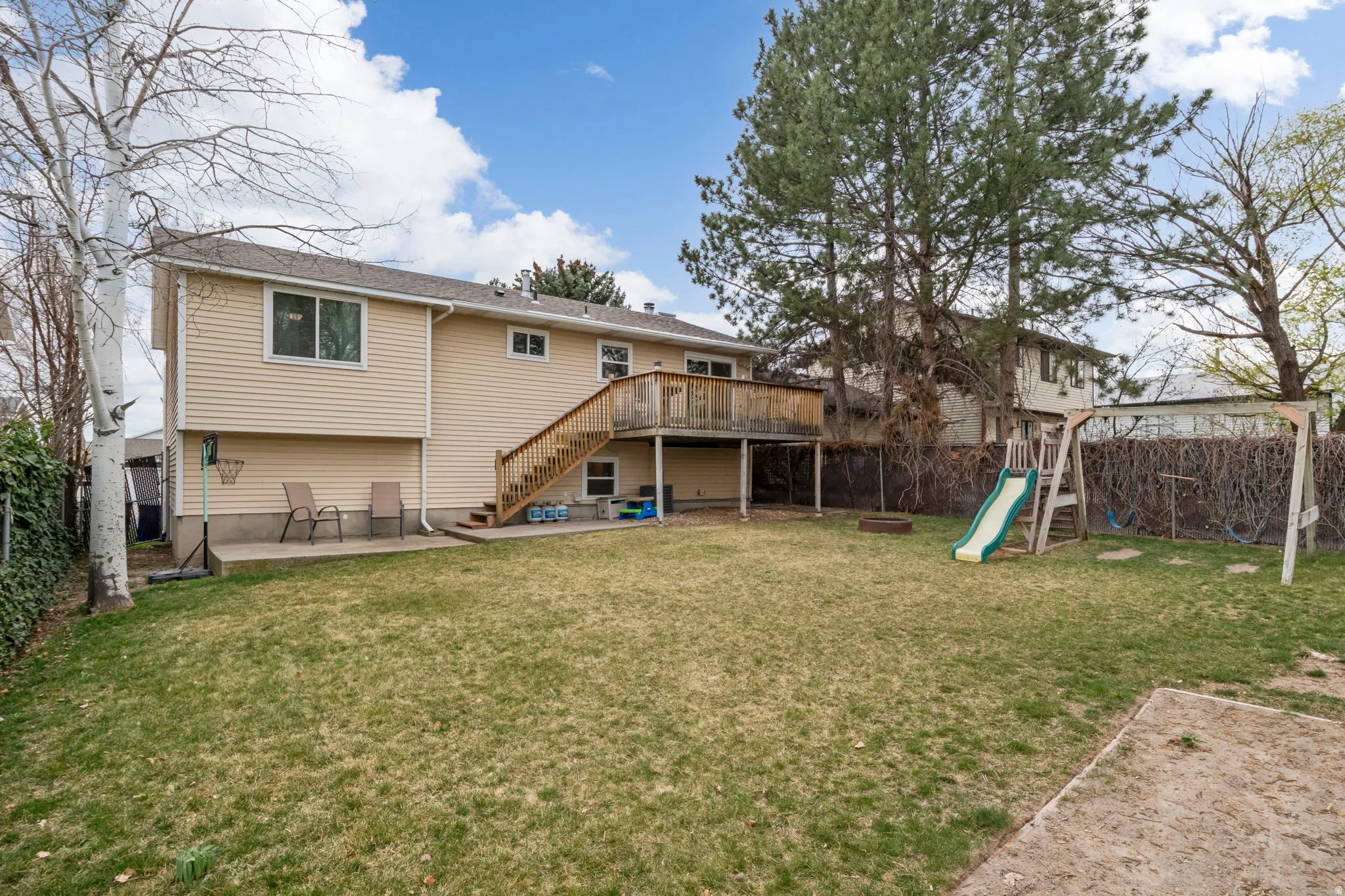 Expansive backyard featuring a manicured lawn, a wooden deck with staircase access, and a concrete patio