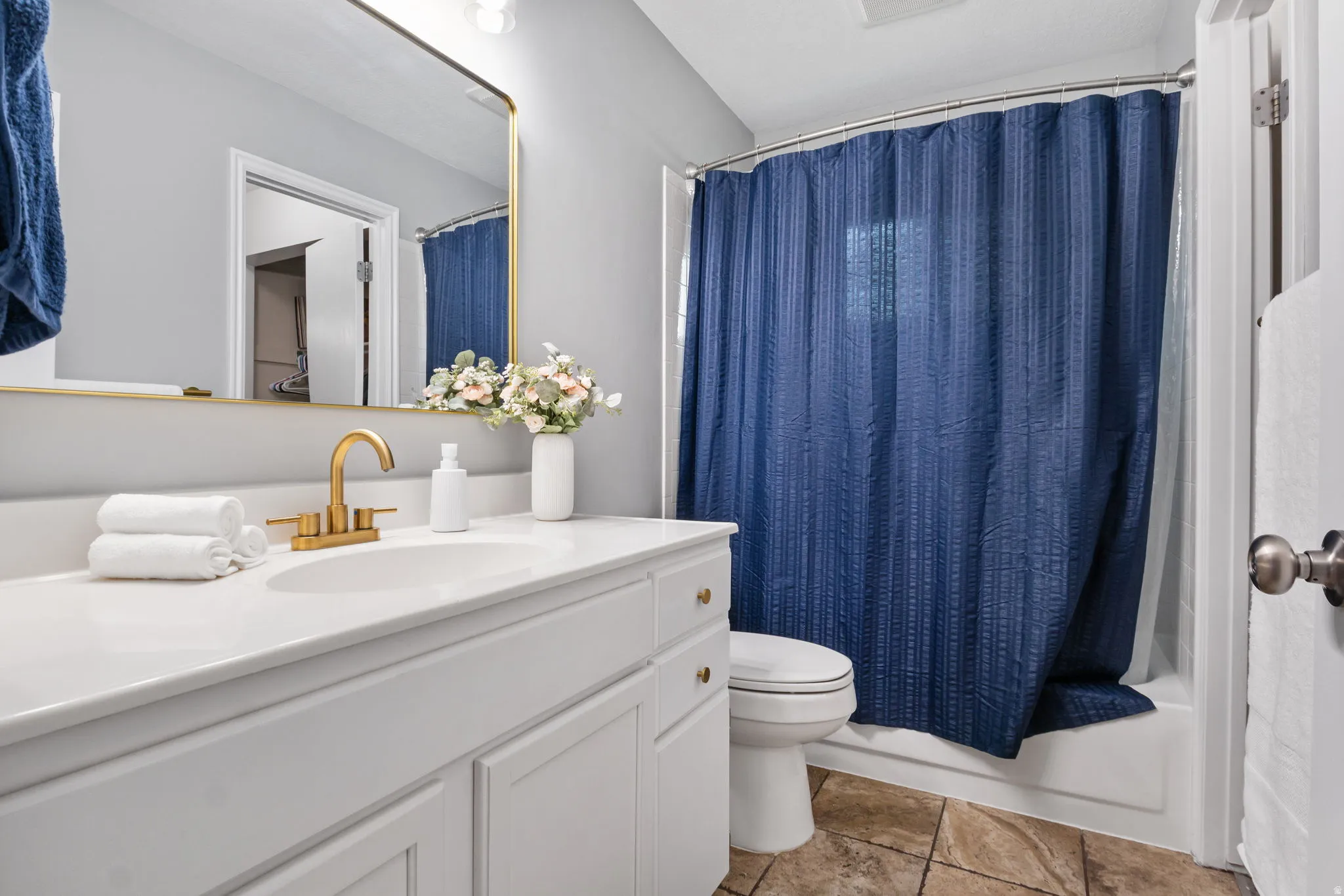 Bathroom featuring a white vanity with integrated sink, brass-finish faucet, framed mirror, and a combination shower-tub with tile flooring