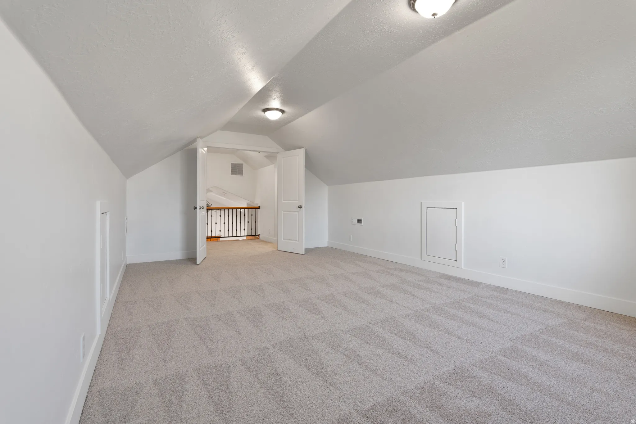 Spacious loft area featuring sloped ceilings and light-toned patterned carpeting