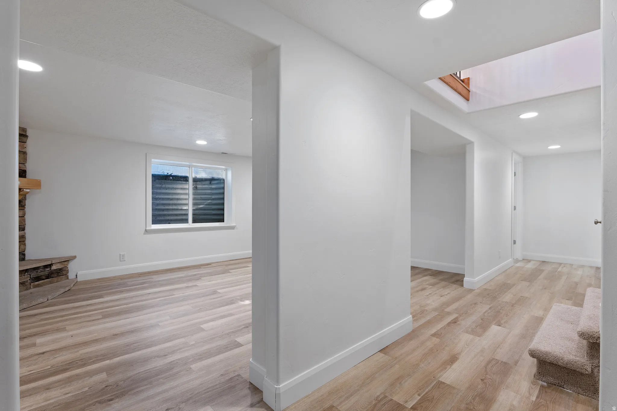 Open concept living area featuring wood-finish flooring, recessed lighting, white baseboards, a stone-clad fireplace with a wood mantel, and a window with horizontal blinds