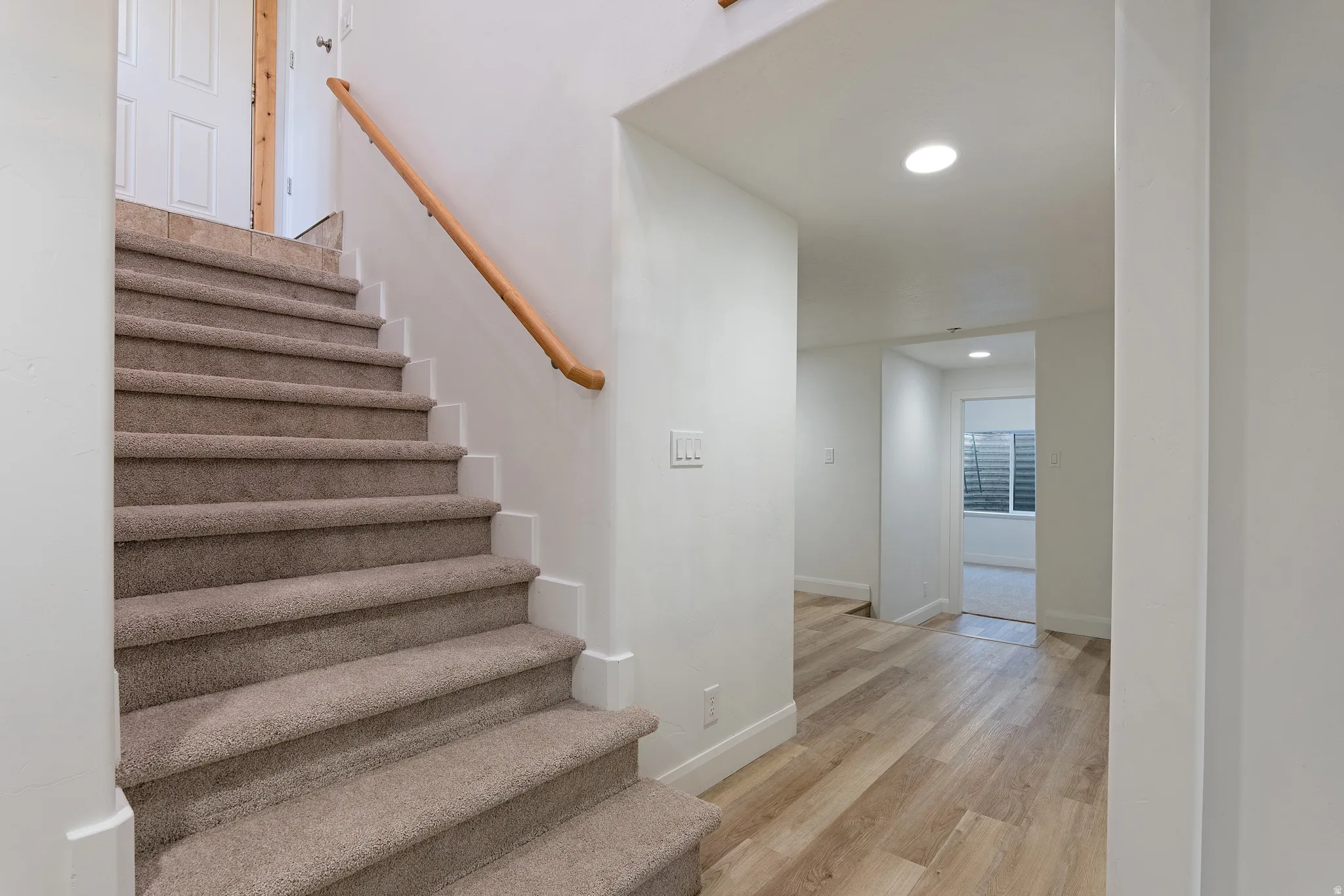 Carpeted staircase with a wood handrail, recessed lighting, and wood-finish flooring in the adjacent hallway
