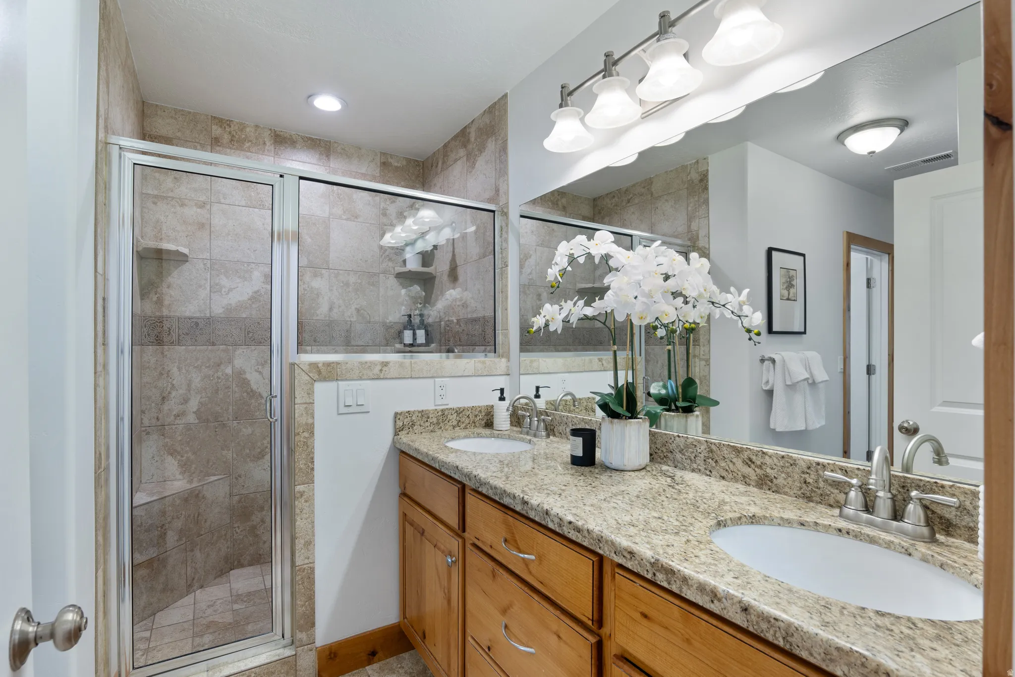 Bathroom featuring a dual vanity with light-toned countertops and undermount sinks, custom wood cabinetry, and a full-width mirror