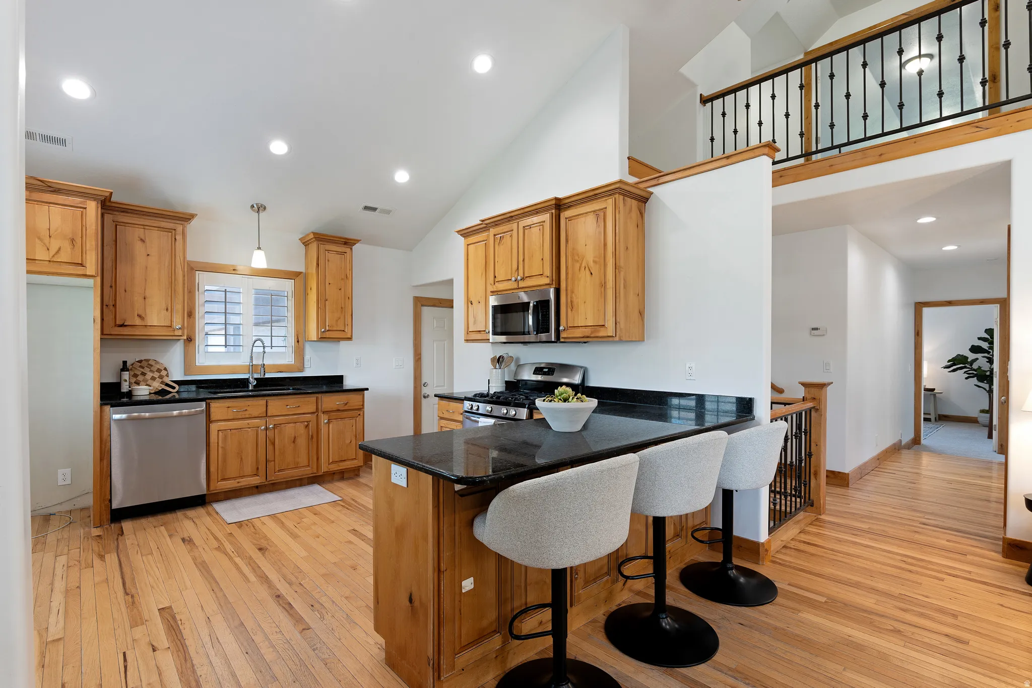 Kitchen featuring natural wood cabinetry, black countertops, stainless steel appliances, and a central island with bar seating