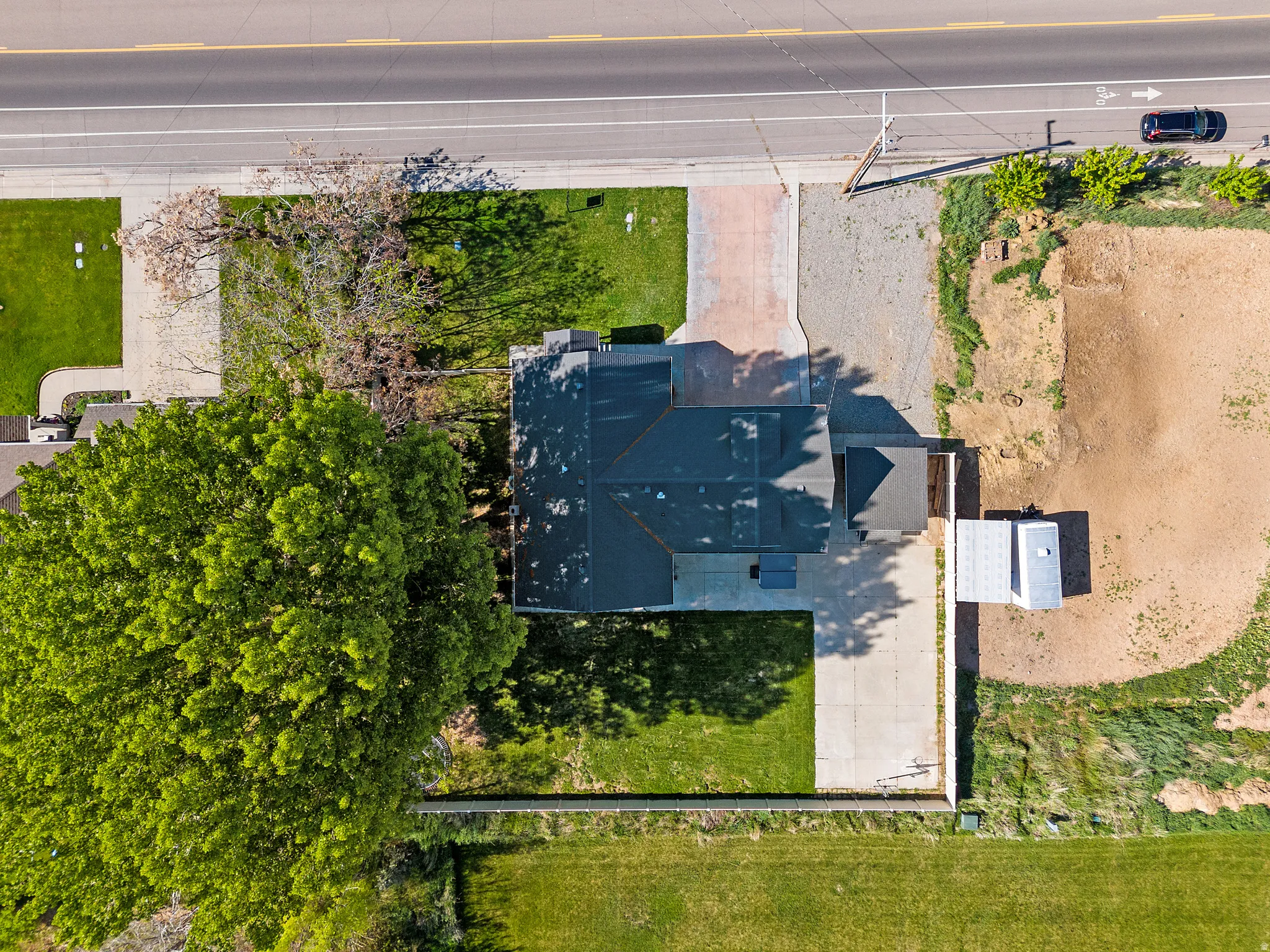 Aerial property overview featuring a dark-toned roof, a paved driveway, and established landscaping