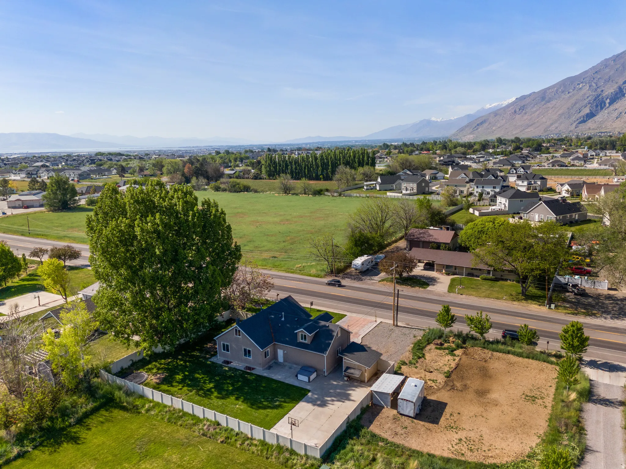 Aerial perspective showcasing a property with a manicured lawn, a paved driveway with a basketball hoop, and two sheds