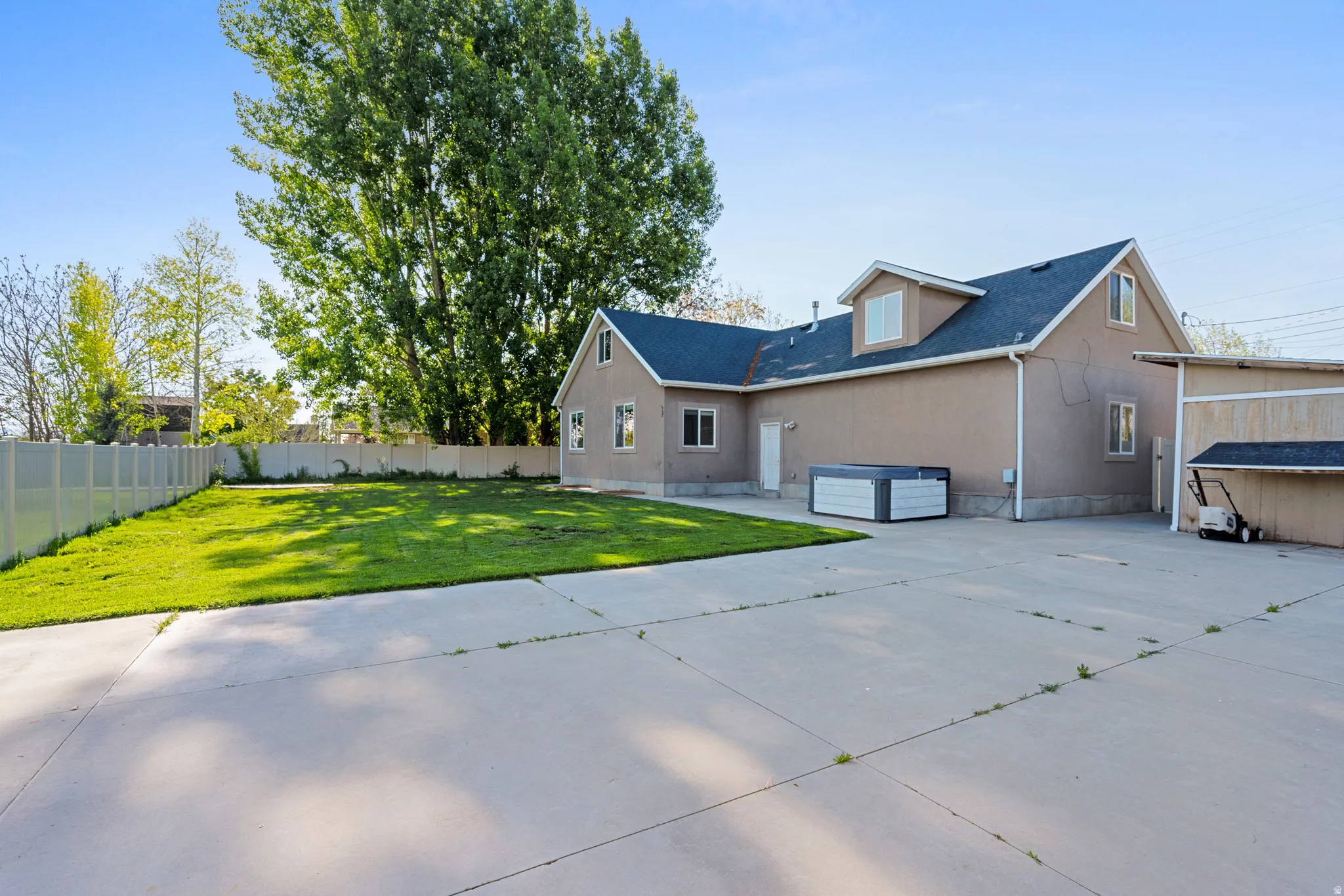 Expansive concrete patio area with a stucco exterior, dormer window, and dark shingle roofing