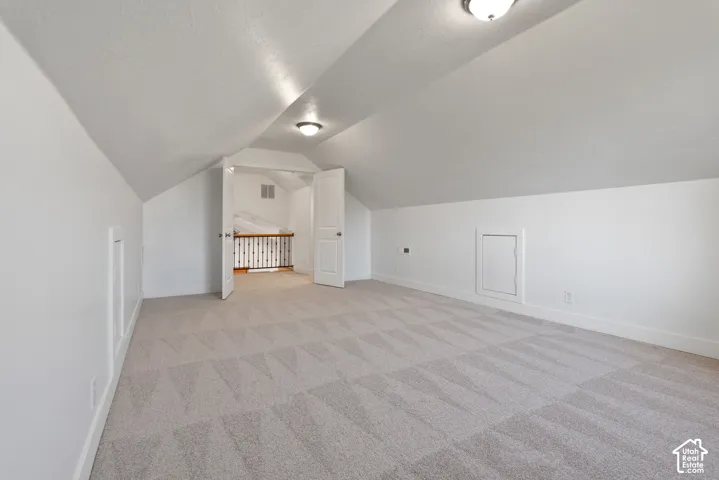 Spacious attic room featuring sloped ceilings, recessed access panels, and neutral-toned patterned carpeting