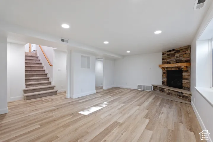 Spacious room featuring wood-finish flooring, recessed lighting, and a corner fireplace with a stone surround and wood mantel