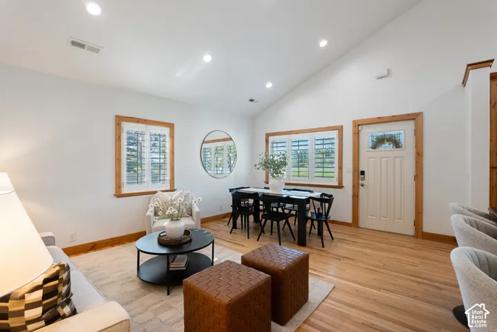 Vaulted ceiling living space featuring wood-finish flooring, wood trim throughout, recessed lighting, and a white paneled entry door with decorative glass