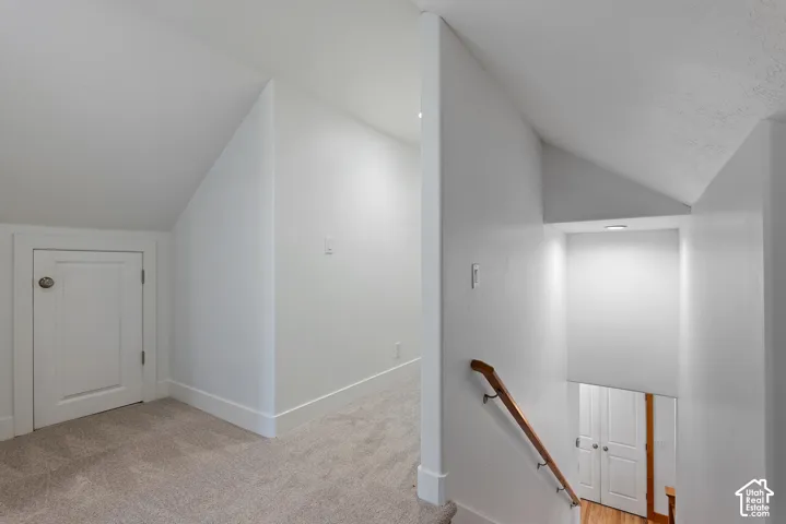 Upper-level landing featuring neutral carpet, white walls, and an angled ceiling