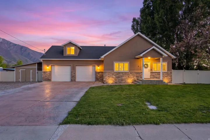 Exterior featuring a two-car garage, stone facade accents, a covered front porch, a well-maintained lawn, and an adjacent storage shed