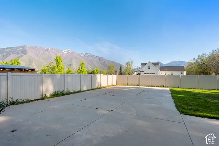 Expansive concrete pad bordered by a white privacy fence and a strip of manicured lawn, with distant mountains forming a scenic backdrop