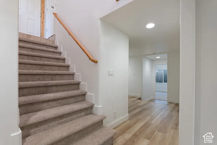Carpeted staircase with wood handrail, light wood-finish flooring, white baseboards, and recessed lighting