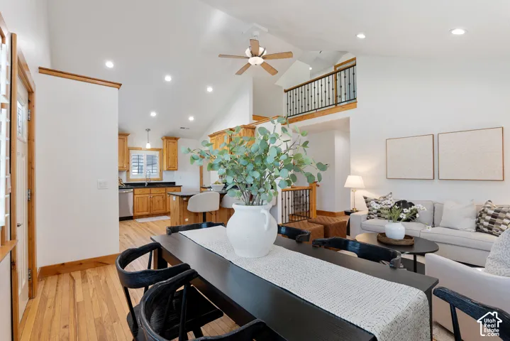 Open-concept living space featuring vaulted ceilings with recessed lighting, wood-finish flooring, a kitchen with wood cabinetry and dark countertops, and a balcony with black wrought iron railing