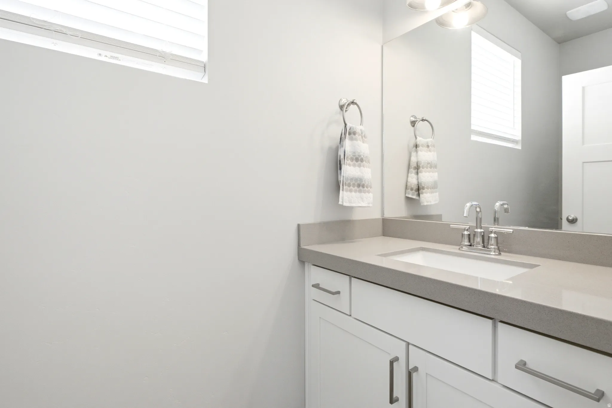 Bathroom vanity featuring an integrated sink, polished chrome faucet, gray countertop, and white shaker-style cabinetry with chrome hardware