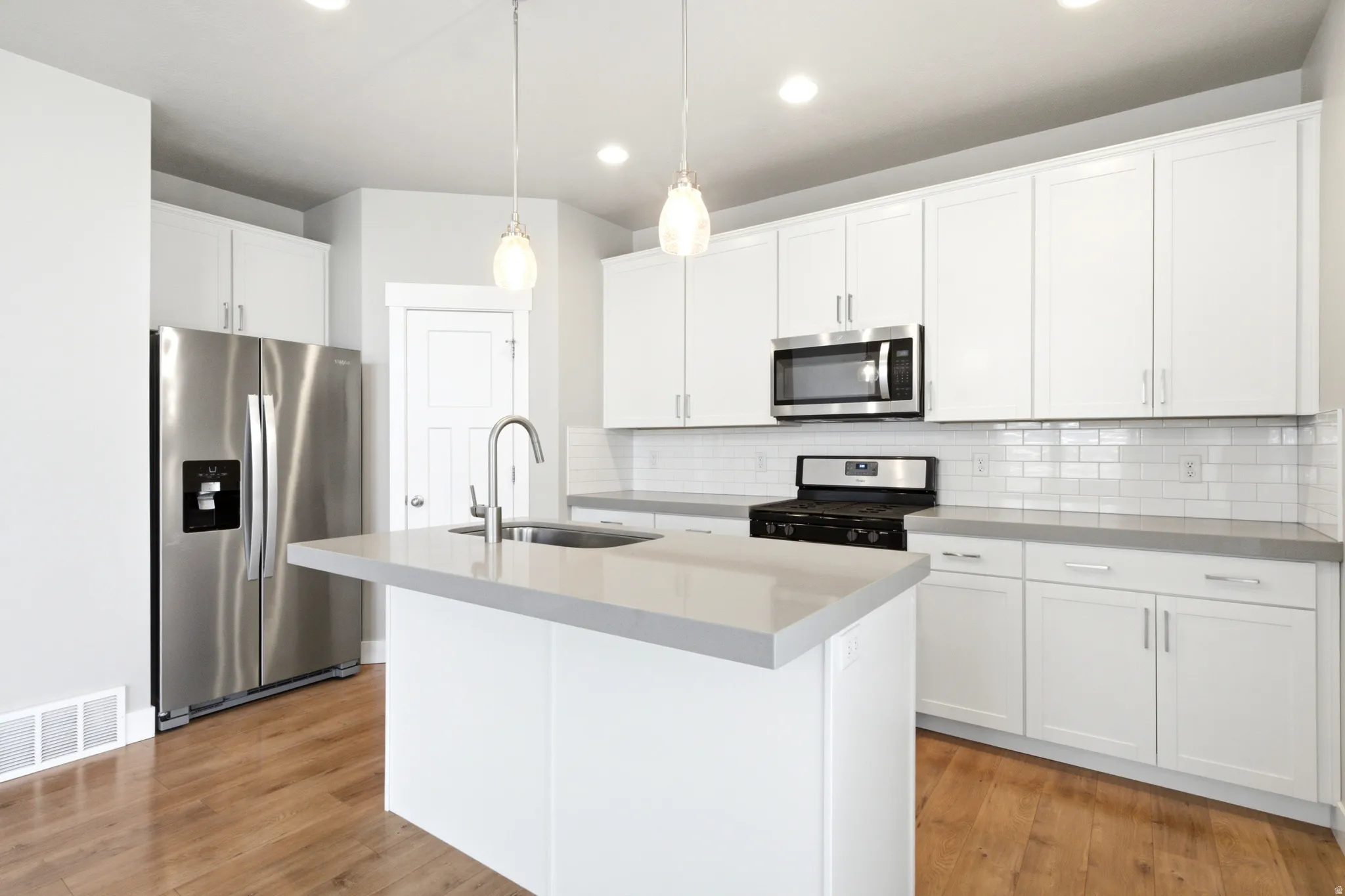 Modern kitchen featuring white cabinetry, stainless steel appliances, a center island with sink, subway tile backsplash, and wood-finish flooring