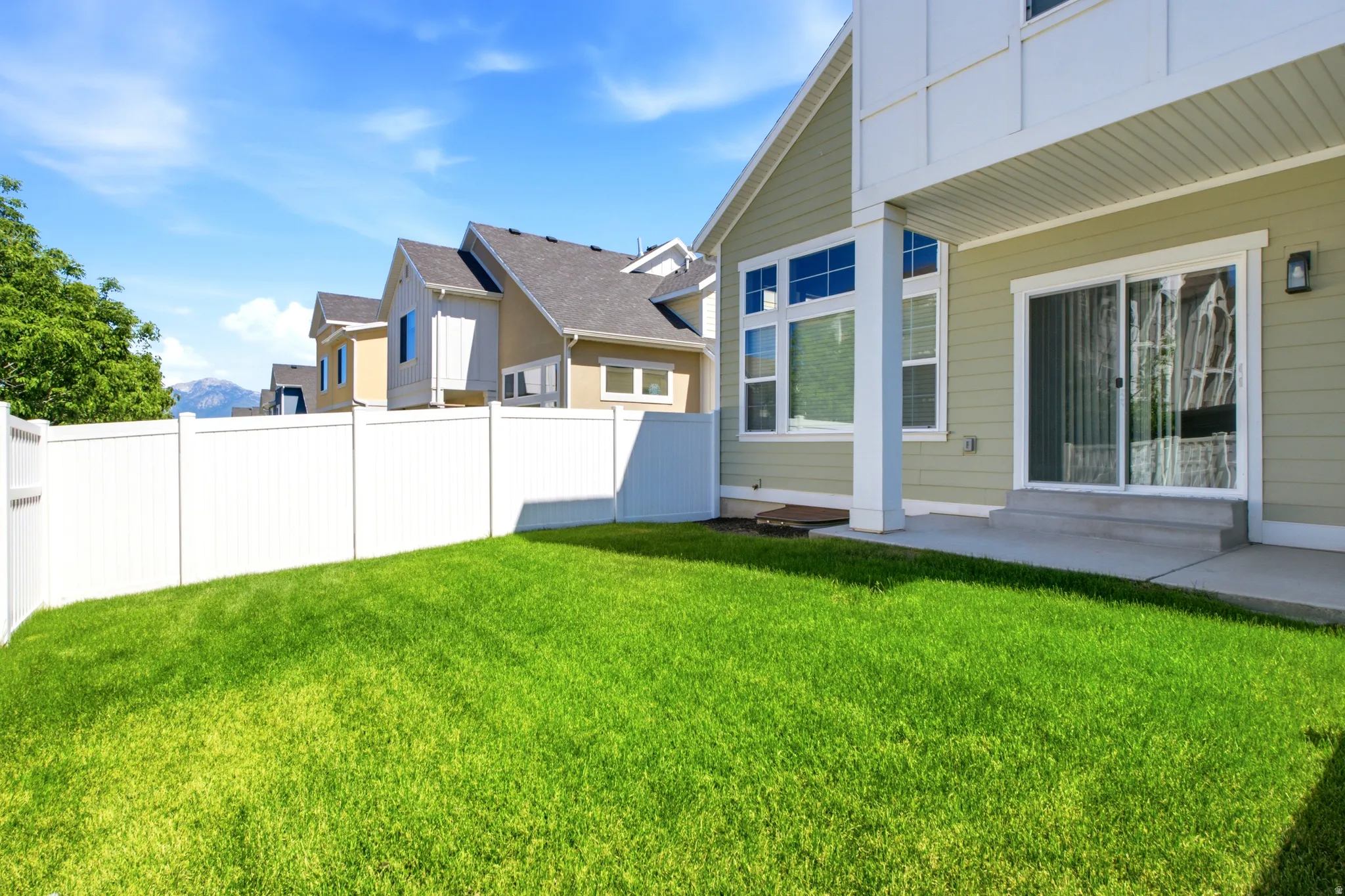 Expansive backyard featuring a green lawn, white privacy fencing, and a concrete patio with sliding glass door access