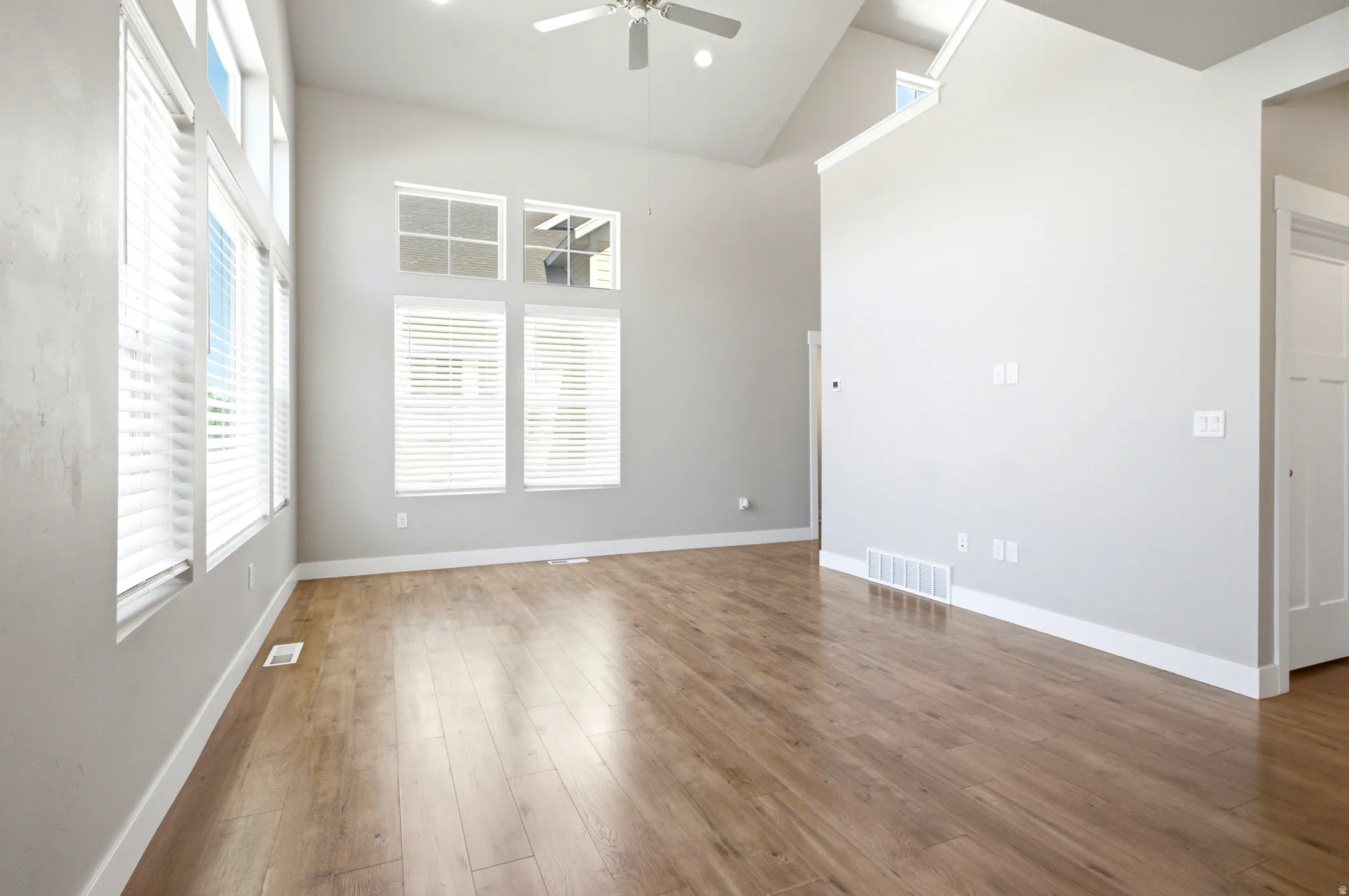 Spacious room featuring vaulted ceilings, wood-finish flooring, a contemporary ceiling fan, and multiple windows with white blinds