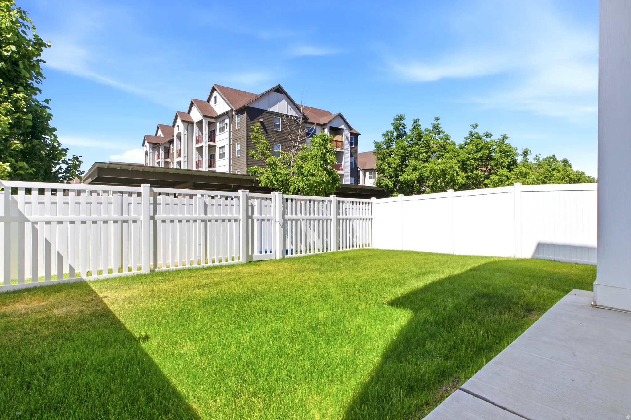 Manicured green lawn bordered by a white picket fence and a solid white privacy fence