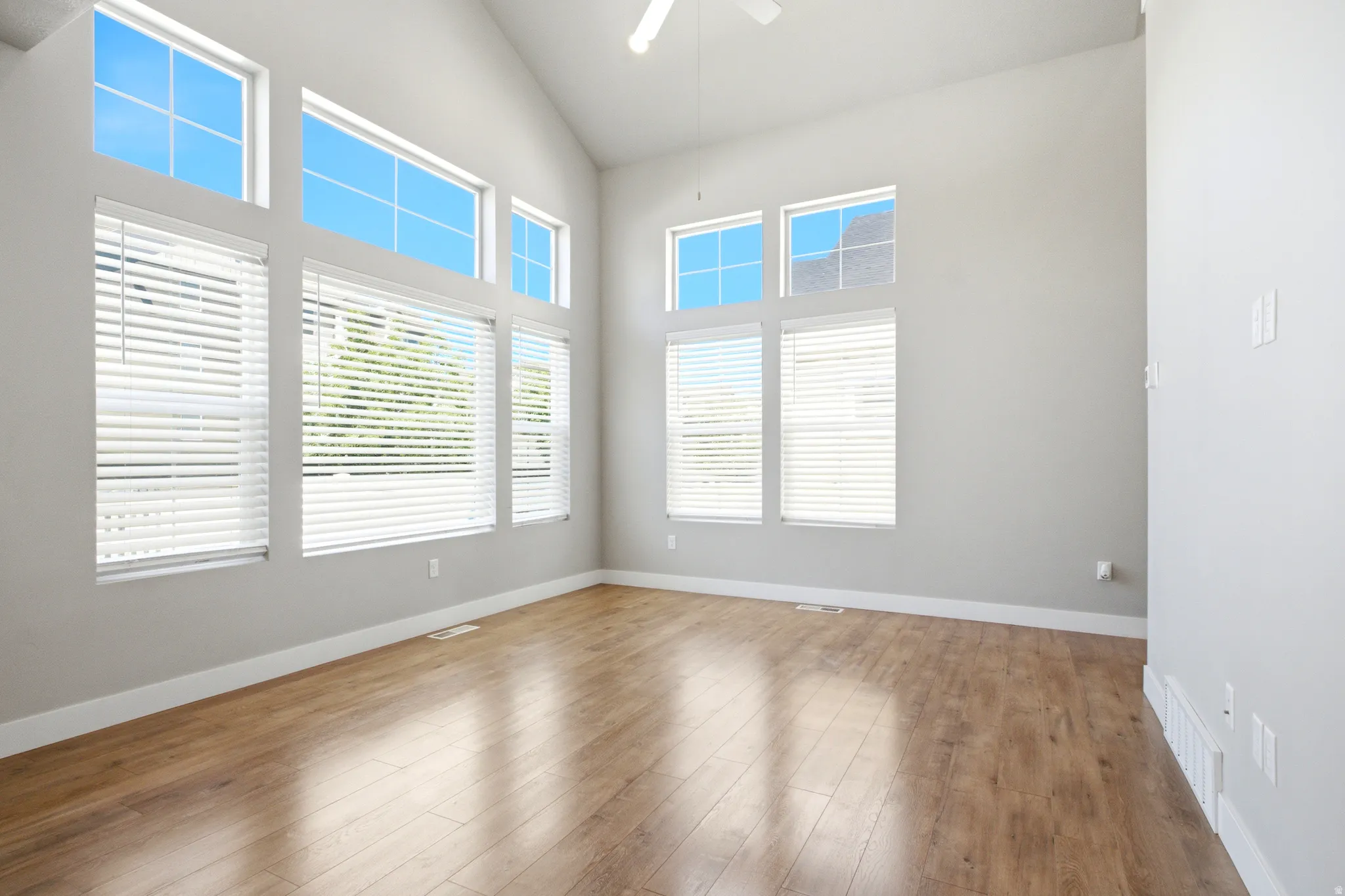 Vaulted ceiling with a ceiling fan, light wood-finish flooring, and multiple windows with white blinds