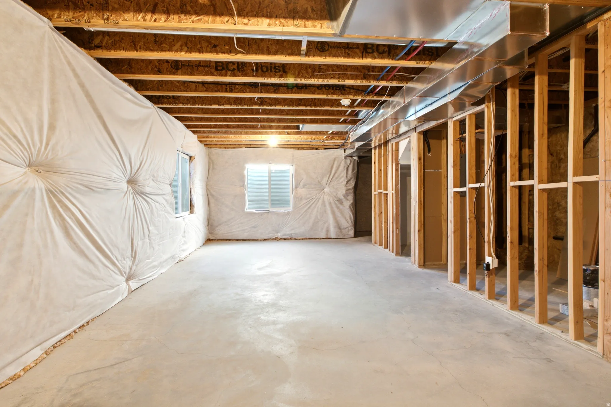 Unfinished basement featuring a concrete floor, framed walls, visible ceiling joists, and two windows with horizontal blinds