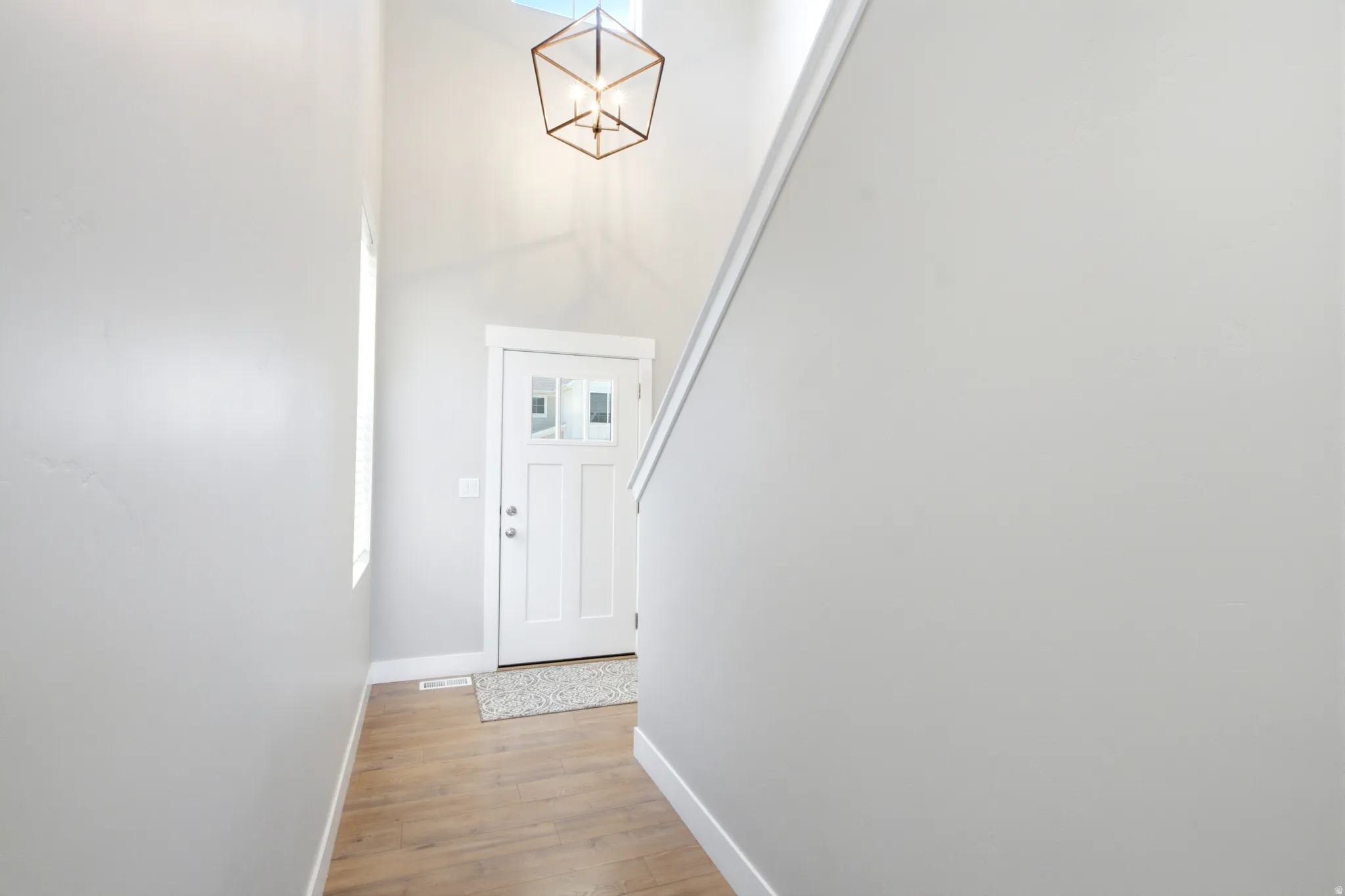 Entryway featuring a white paneled door with glass inserts, wood-finish flooring, a high vaulted ceiling, and a geometric pendant light fixture