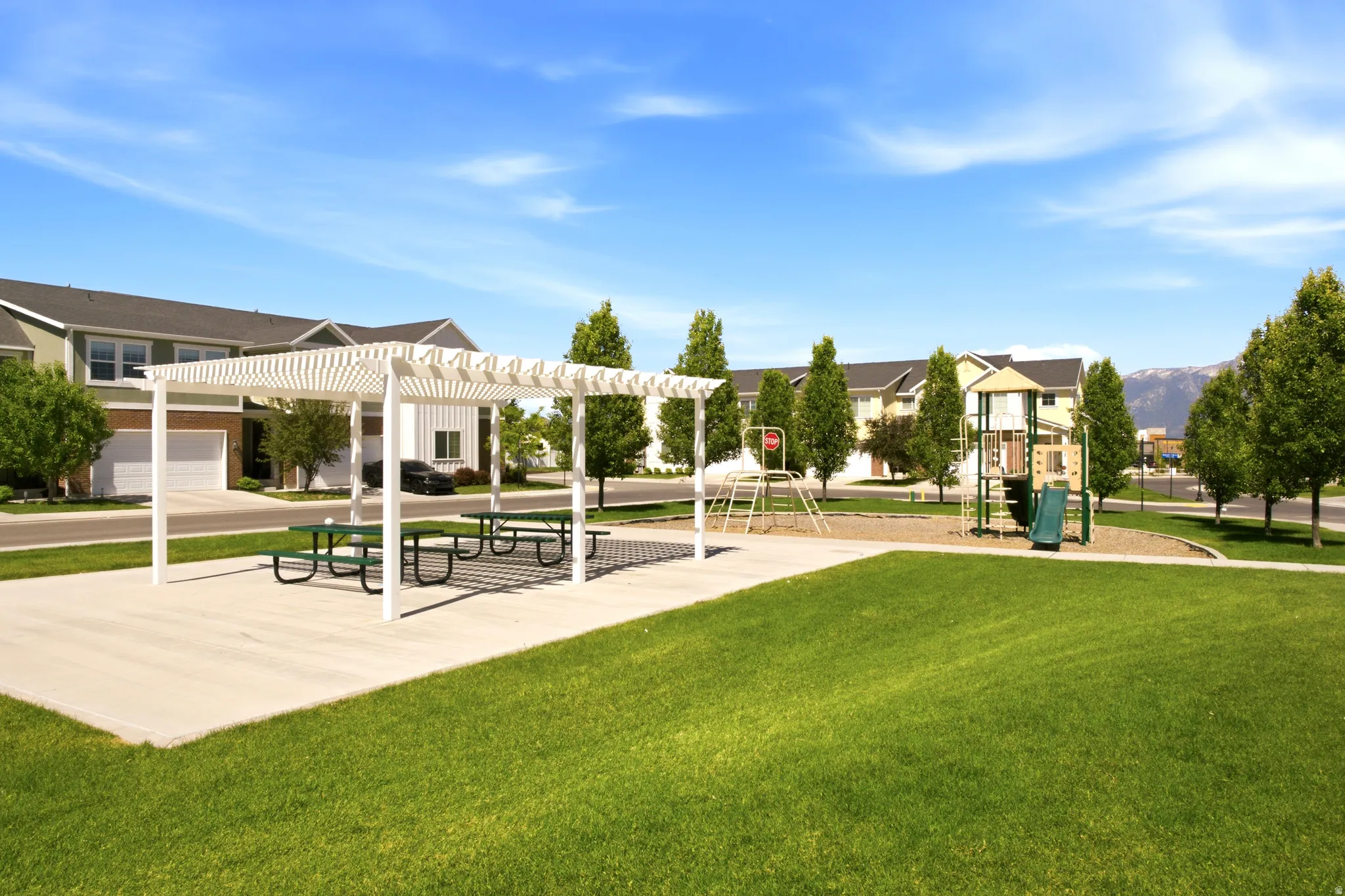 Community green space featuring a white pergola, picnic tables, and a playground