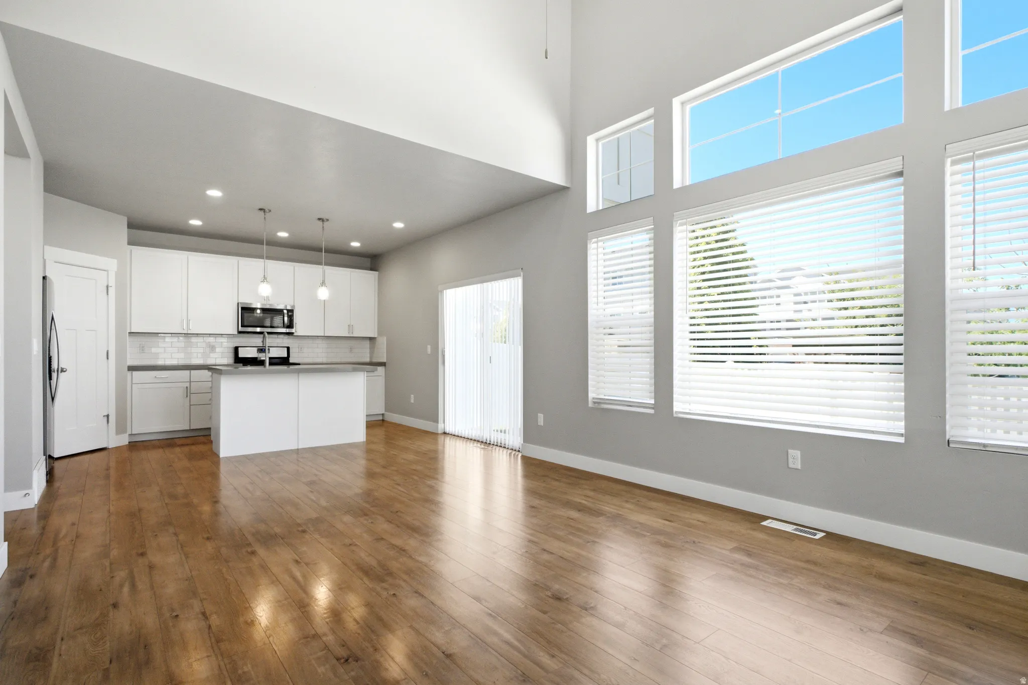 Open-concept living space featuring wood-finish flooring, a kitchen with white cabinetry and an island, a sliding glass door, and a wall of tall windows