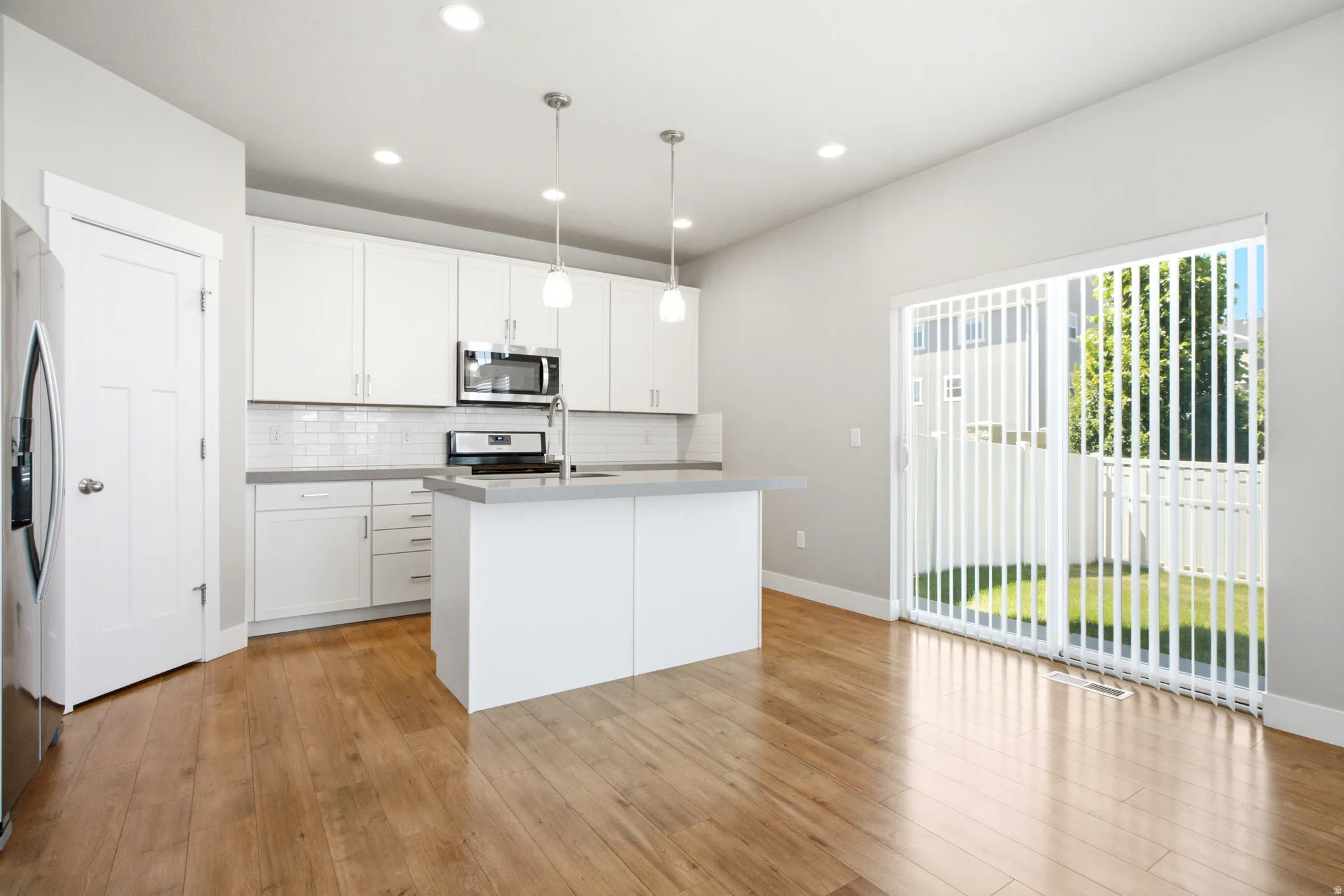 Bright kitchen featuring white cabinetry, subway tile backsplash, stainless steel appliances, a center island with sink, and wood-finish flooring