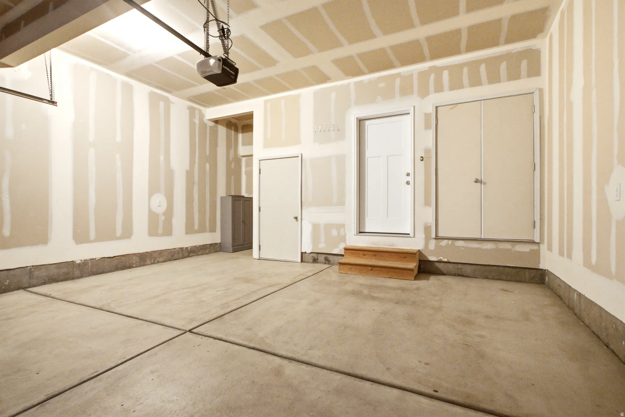 Spacious garage featuring a finished concrete floor, unfinished drywall, overhead garage door opener, and a built-in step with a white door