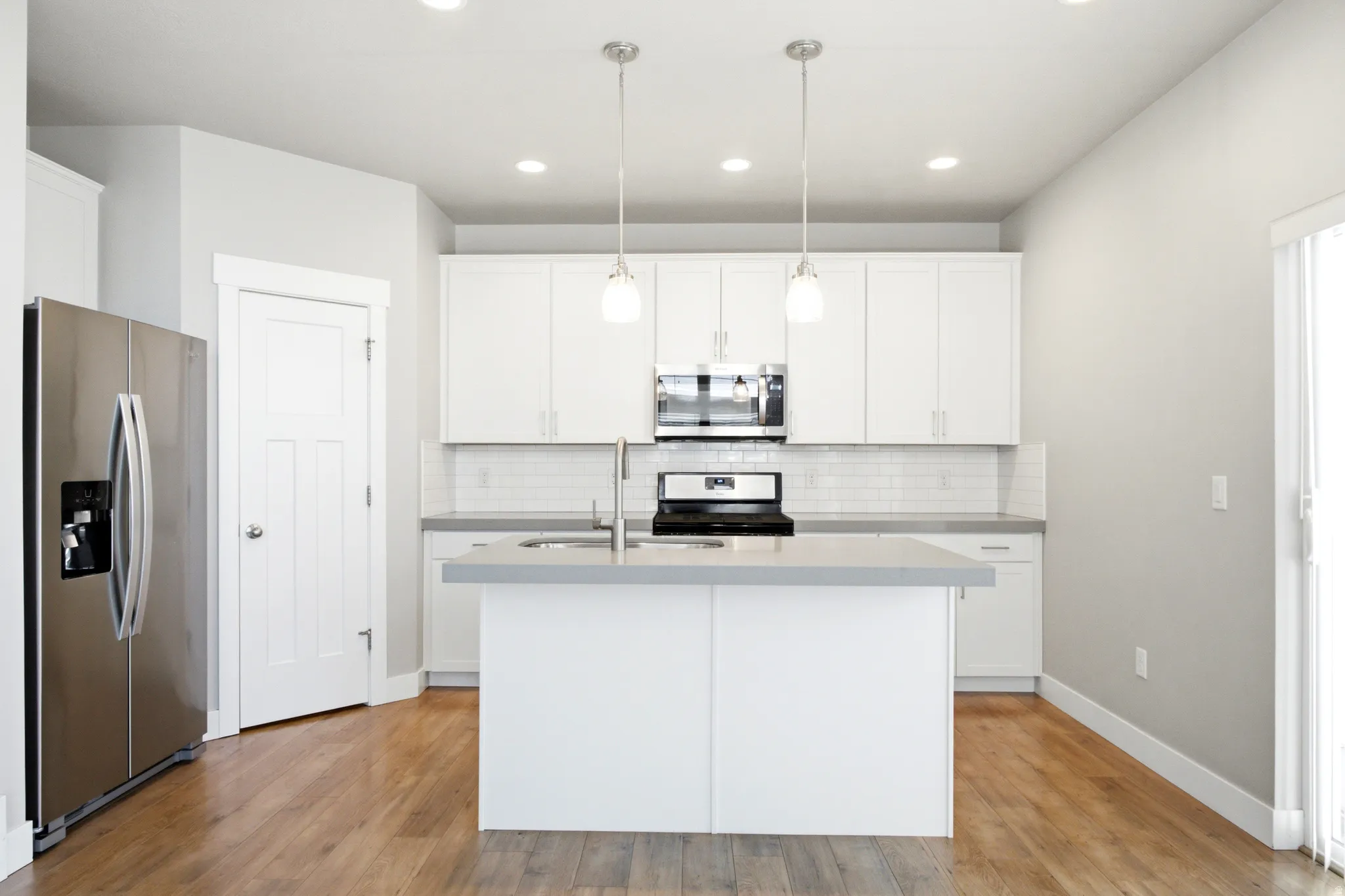 Modern kitchen with wood-finish flooring, white cabinetry, and light gray countertops