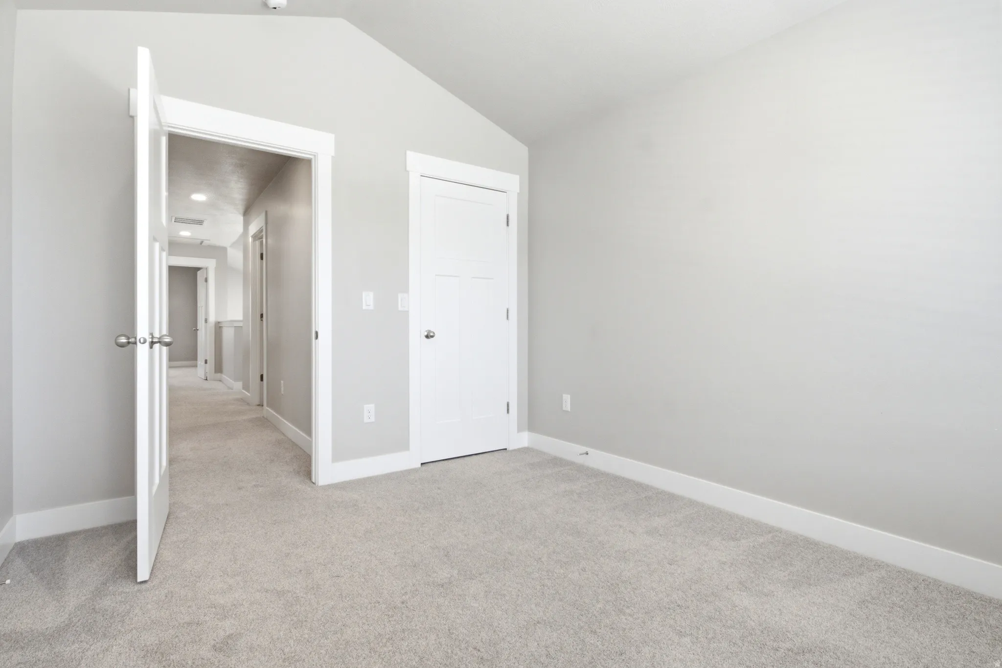 Spacious room featuring vaulted ceilings, light gray wall paint, white trim, and plush carpeting