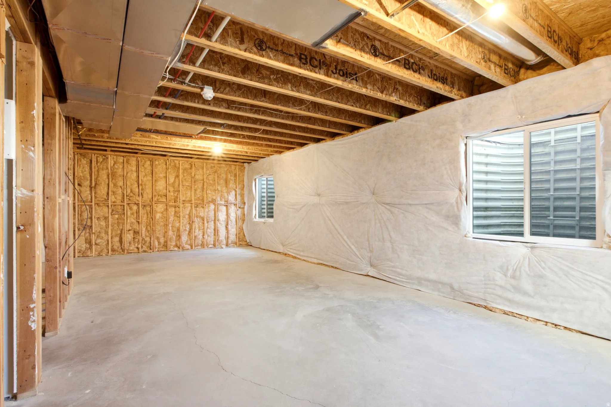 Unfinished lower level featuring concrete flooring, exposed wood joists, and two egress windows
