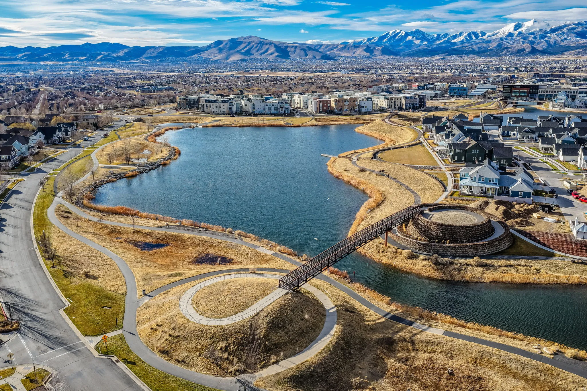Expansive community lake with a pedestrian bridge and surrounding walking paths