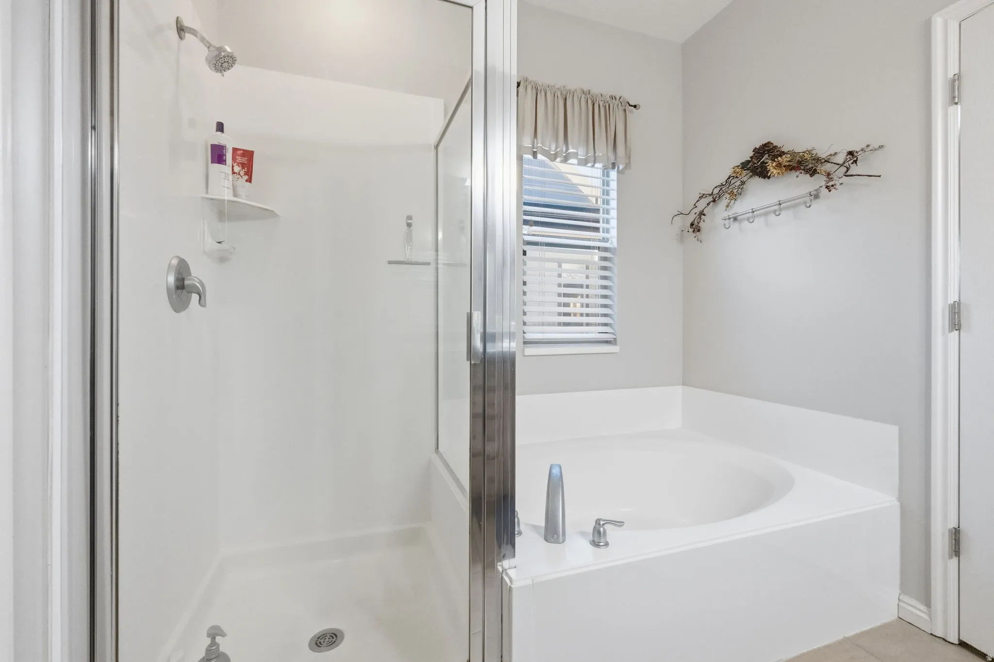 White acrylic corner soaking tub with chrome fixtures, accompanied by a separate glass-enclosed shower with a handheld showerhead