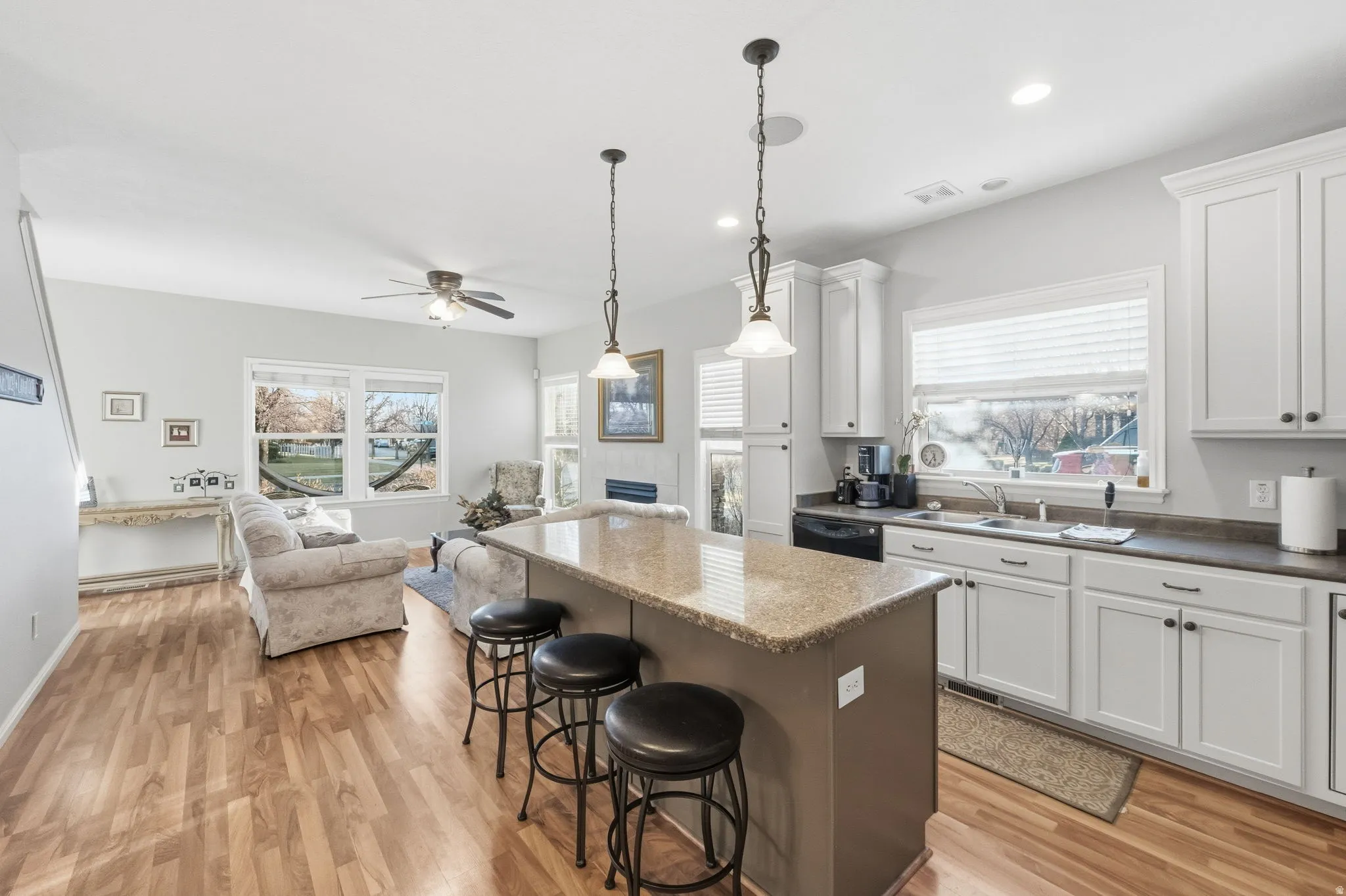 Open-concept living space featuring a kitchen island with seating, white cabinetry, wood-finish flooring, and a living area with large windows