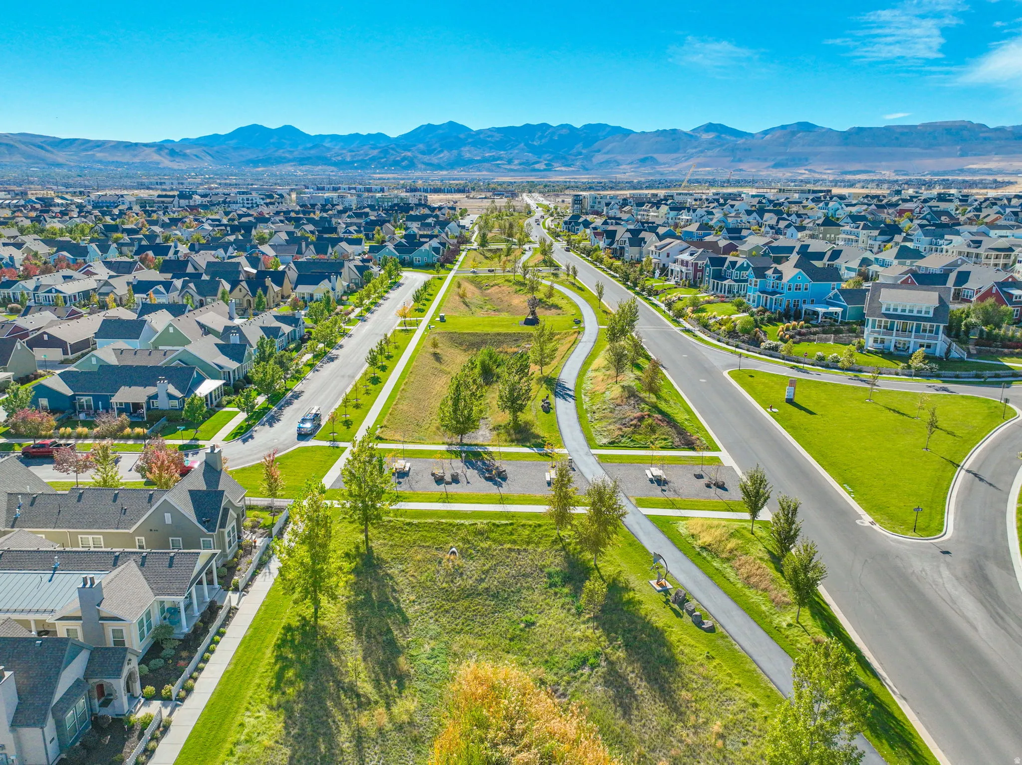 Expansive residential area with diverse architectural styles, clear skies, mountain backdrop, and green common areas with walking paths